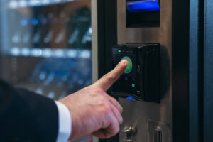 Close up hand of man pushing button on vending machine for choosing a snack or drink. Small business and consumption concept.